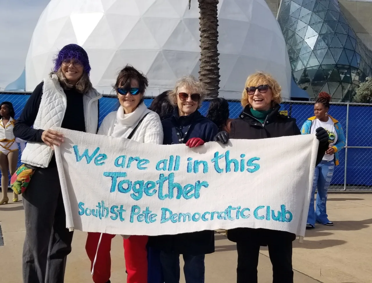 Four MLK Parade participants holding a South St. Petersburg Democratic Club banner that reads We are all in this together.
